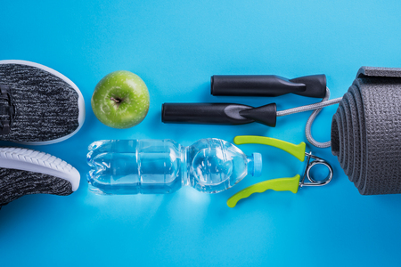 Sport shoes, bottle of water, apple and yoga mat with copy space on blue background.の写真素材