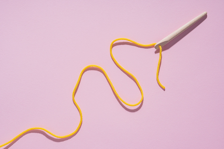 Needle and yellow thread on a pink background.の写真素材
