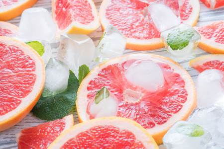 Red grapefruit slices, ice and mint on a white wooden background.の写真素材