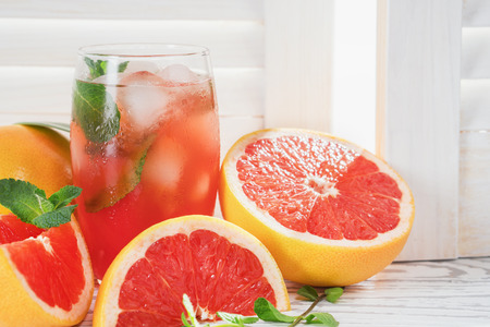 Fresh grapefruits and glass of grapefruit juice with ice and mint on rustic white wooden table opposite the blinds with copy space. Close-up.の写真素材