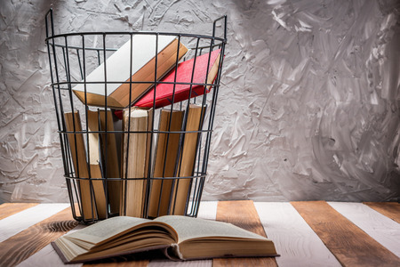 Old books in a metal basket on a wooden table. Old book open on a wooden table. Education, leisure concept.の写真素材