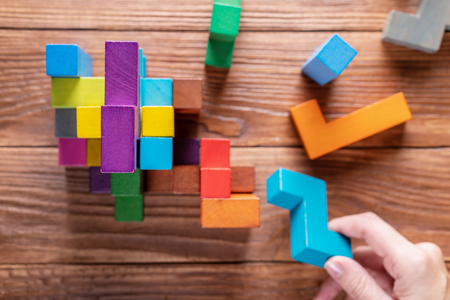 Concept of decision making process, logical thinking. Logical tasks. Conundrum, find the missing piece of the proposed. Hand holding wooden puzzle element. Hand sets the last element of the puzzle.の写真素材