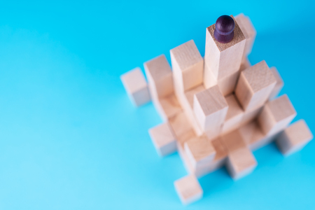 Abstract construction from wooden blocks with copy space on blue background. Business metaphor, abstract person on top of a career. The concept of success, achievement, victory.の写真素材