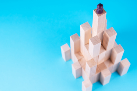 Abstract construction from wooden blocks with copy space on blue background. Business metaphor, abstract person on top of a career. The concept of success, achievement, victory.の写真素材