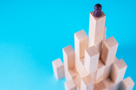 Abstract construction from wooden blocks with copy space on blue background. Business metaphor, abstract person on top of a career. The concept of success, achievement, victory.の写真素材