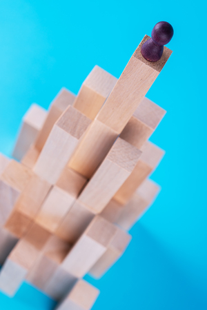 Abstract construction from wooden blocks with copy space on blue background. Business metaphor, abstract person on top of a career. The concept of success, achievement, victory.の写真素材