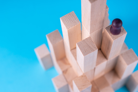 Abstract construction from wooden blocks with copy space on blue background. Business metaphor, abstract person on top of a career. The concept of success, achievement, victory.の写真素材