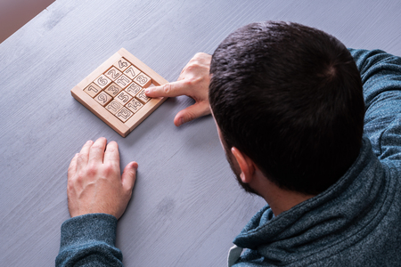 Top view on man's hand solves the conundrum on the gray wooden table background, close up. The concept of concentration, logical thinking.の写真素材