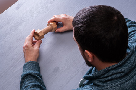 Top view on man's hand tightens the bolt and nut. Build and repair concept, wooden bolt and hex nut.の写真素材