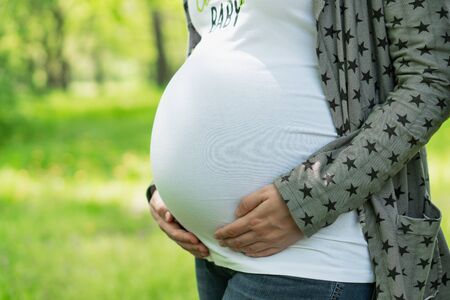 Young pregnant woman in the park. Happy pregnant woman stroking her belly. Woman at 39 weeks gestation (9 month).の写真素材