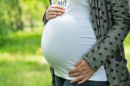 Young pregnant woman in the park. Happy pregnant woman stroking her belly. Woman at 39 weeks gestation (9 month).の写真素材