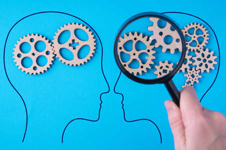 Human brain is made gear mechanism on blue background. The brain is viewed through a magnifying glass. Two different thought processes, concept of different thinking.の写真素材