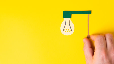 Man hand turns on incandescent light bulb. Energy concept with light bulb on yellow background with copy spaceの写真素材