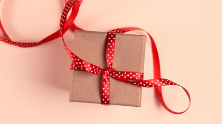 Gift box with red ribbon over pink paper background with copy spaceの写真素材
