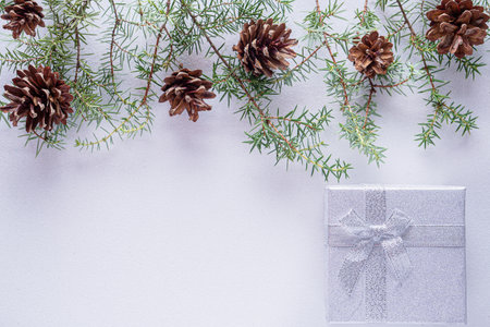 Christmas white background with glitter silver gift box and fir branches and cones with copy space. Christmas wallpaper concept. top viewの写真素材