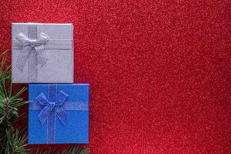 Christmas red background with two glitter gift box and fir branches and cones with copy space. Christmas wallpaper concept. top viewの写真素材