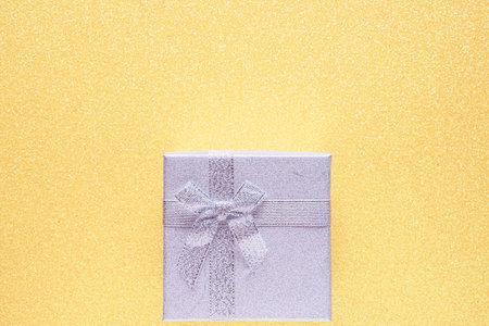 Silver gift box on glitter light yellow background with copy space. close up. top view. birthday...