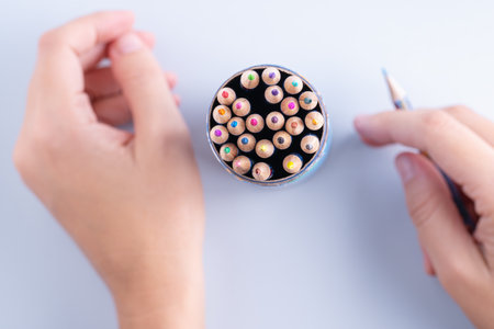 Set of colorful pencils and woman's hand holding a pencil on a light blue background. Creativity, creative arts and crafts activities abstract conceptの写真素材