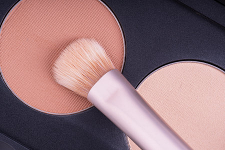 A palette with eye shadows and a makeup brush. Brush gains beige eyeshadows on pile to be used in make-up. Cosmetic swatch of eyeshadows, powder, bronzer or highlighter in brown-beige colorsの写真素材