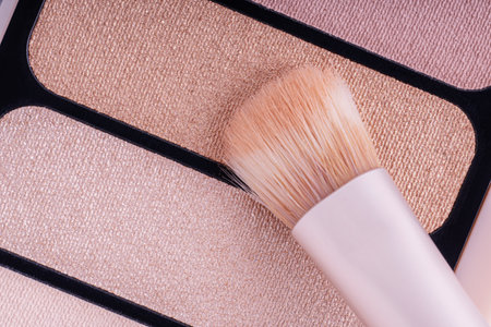 A palette with eye shadows and a makeup brush. Brush gains beige eyeshadows on pile to be used in make-up. Cosmetic swatch of eyeshadows, powder, bronzer or highlighter in brown-beige colorsの写真素材