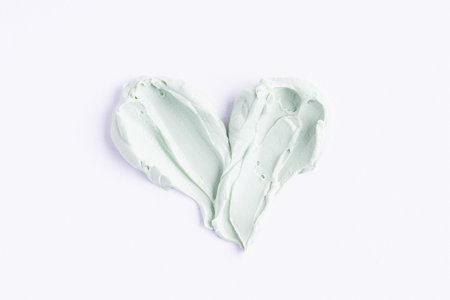 Green clay mask or correcting concealer smear smudge in the shape of a heart on white background.の写真素材
