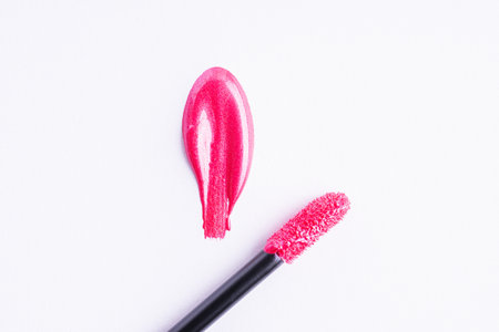 Pink shiny liquid lipstick in heart shape and applicator isolated on white background. Swatch of deep pink lip gloss. Top view, flat lay, copy spaceの写真素材