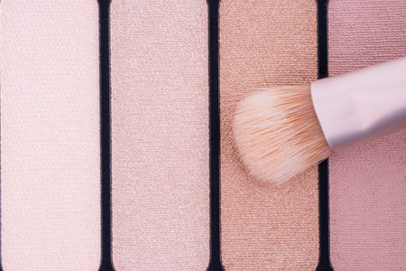A palette with eye shadows and a makeup brush. Brush gains beige eyeshadows on pile to be used in make-up. Cosmetic swatch of eyeshadows, powder, bronzer or highlighter in brown-beige colorsの写真素材