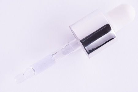 Pipette with serum oil on white background. Dropper pipette with transparent light purple drops with bubbles. Gel, oil, acid cosmetic productの写真素材