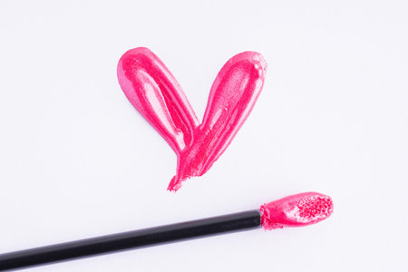 Pink shiny liquid lipstick in heart shape and applicator isolated on white background. Swatch of deep pink lip gloss. Top view, flat lay, copy spaceの写真素材
