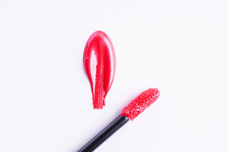 Red shiny liquid lipstick in heart shape and applicator on white background. Swatch of deep red lip gloss. Top view, flat lay, copy spaceの写真素材