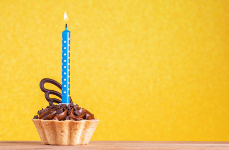 Birthday cupcake on yellow background with copy space. Caramel cupcake with single blue candleの写真素材