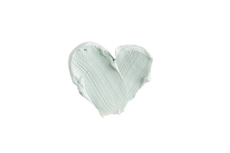 Green clay mask or correcting concealer smear smudge in the shape of a heart isolated on white background. Cream texture. Facial mask, skincare beauty product swatch closeup. SPA backgroundの写真素材