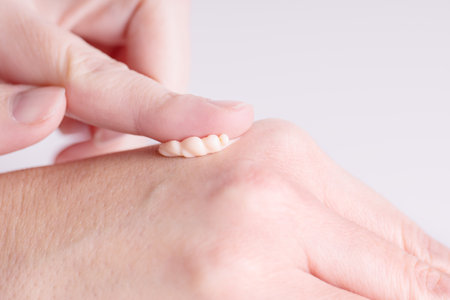 Female hands care. Close up of woman applying cream on hand skin. Skin care cosmetics in peach fuzz color, moisturizing gel.の写真素材
