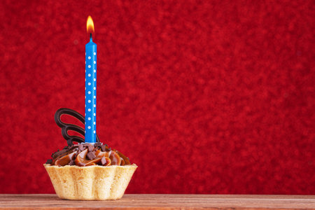 Birthday cupcake on red background with copy space. Caramel cupcake with single blue candleの写真素材