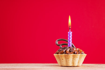 Birthday cupcake on red background with copy space. Caramel cupcake with single purple candleの写真素材