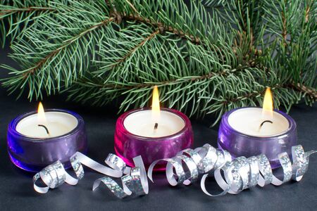 christmas tree branch with three burning candle and ribbon over black background の写真素材