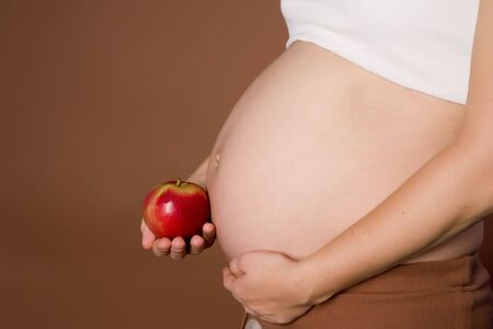 Pregnant woman holding apple on brown ground