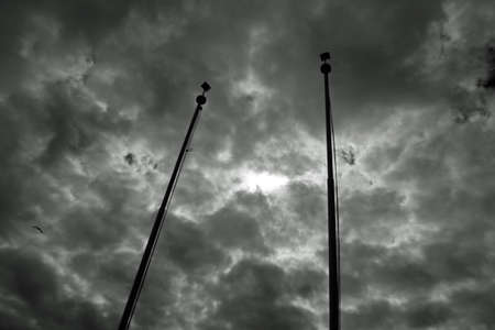 Dramatic dark sky full of clouds with sun reflection between two polesの写真素材