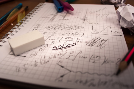 Notebook full of written formulas with pencil and eraser on top of it. Crumpled paper all around the...