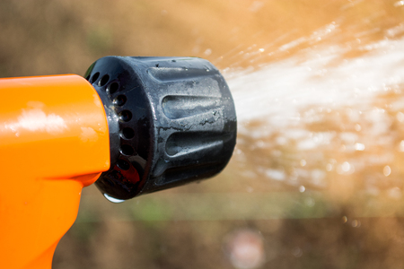 Closeup of hand held sprinkler with water spraying on the fieldの写真素材