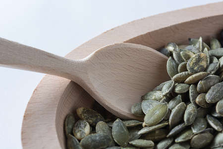 Pumpkin seeds in wooden bowl with wooden spoon isolated on white backgroundの写真素材