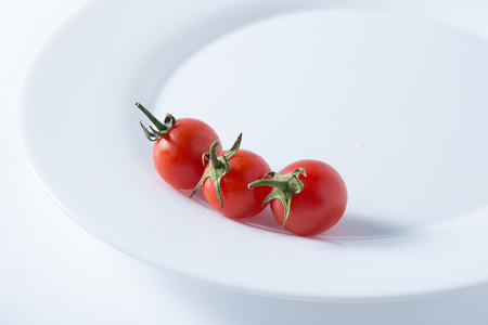 Ripe and red cherry tomatoes in white plate isolated on white backgroundの写真素材