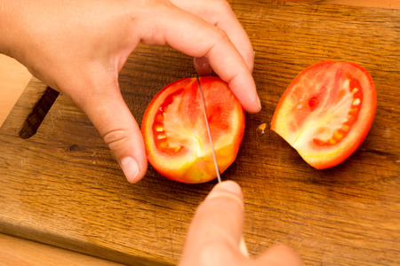 Cutting and chopping  tomato on a wooden plate. Preparing it for a saladの写真素材