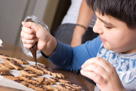 New year and happy family concept. Kid making decoration on gingerbread cookie close up. Baking with childrenの写真素材