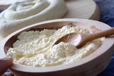 Molten cheese prepared for the cheese pie in the wooden bowl with spoon and female hand holding it. On the backround visible rolled cheese pie ready for bakingの写真素材