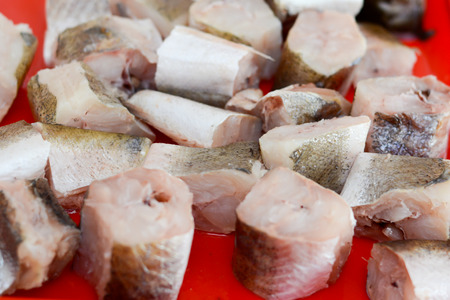 Fish hake sliced and chopped and prepared to be baked on the red plateの写真素材