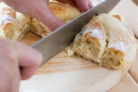 Female hands cut freshly baked cheese pie on the wooden plateの写真素材