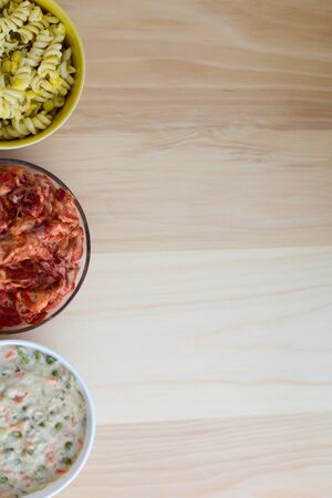 Pasta salad, pepper salad and russian salad in ceramic bowls isolated on wooden table with copy spaceの写真素材
