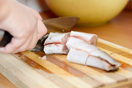 Female hands with knife slicing fish hake on wooden plate.の写真素材