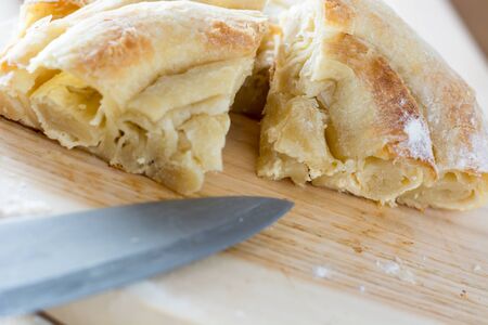Fresh and delicious cheese pie cut on the wooden plate ready to be served to the guests, with knife visible on the wooden plateの写真素材